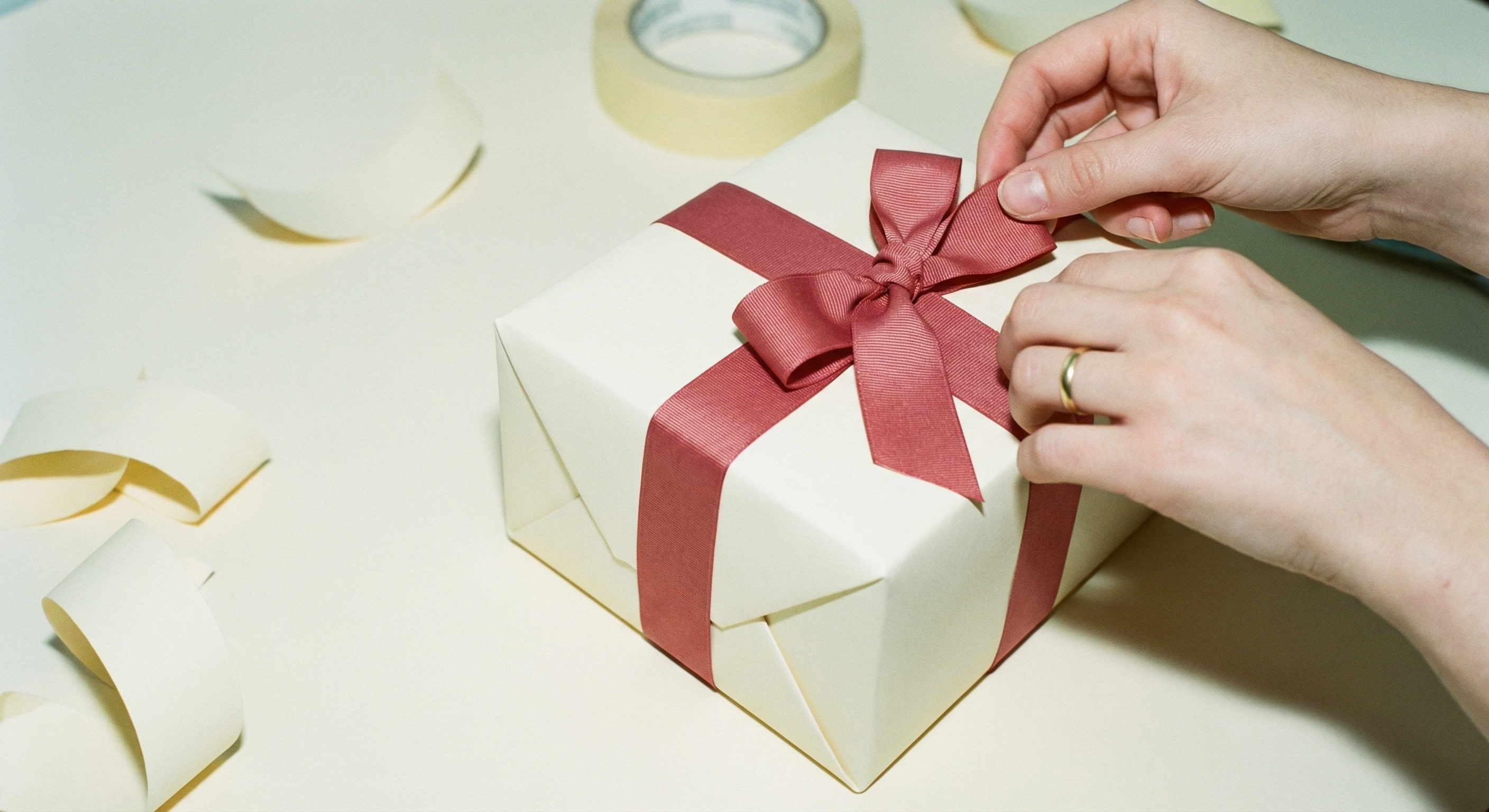 Three-quarter angle view of a perfectly wrapped rectangular gift box in cream paper with a bold red ribbon and simple bow
